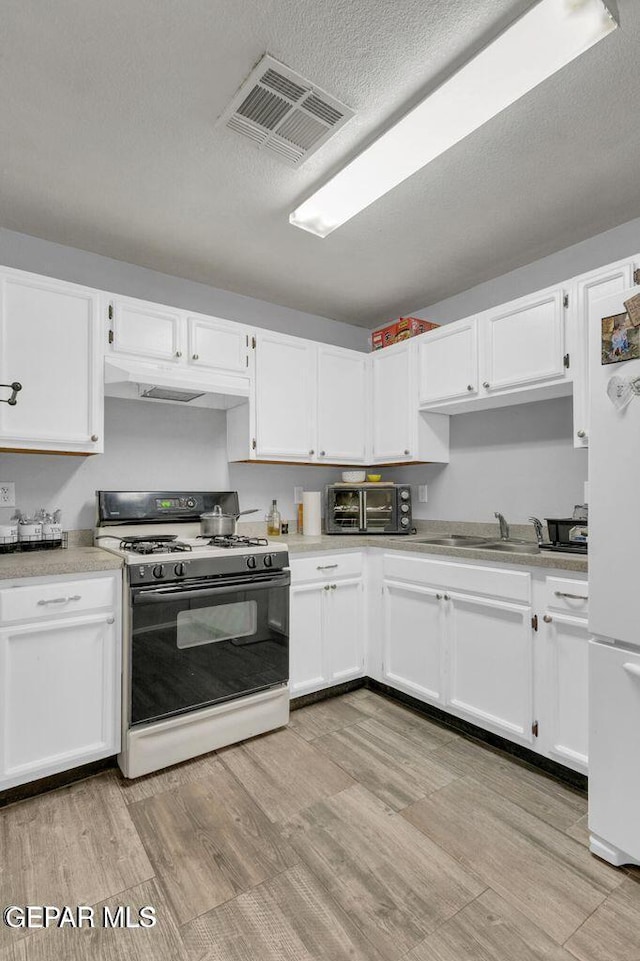 kitchen with white appliances, a textured ceiling, white cabinets, light hardwood / wood-style floors, and sink