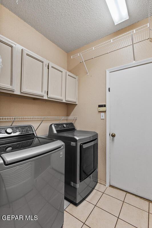 laundry room with cabinets, washing machine and dryer, light tile patterned floors, and a textured ceiling