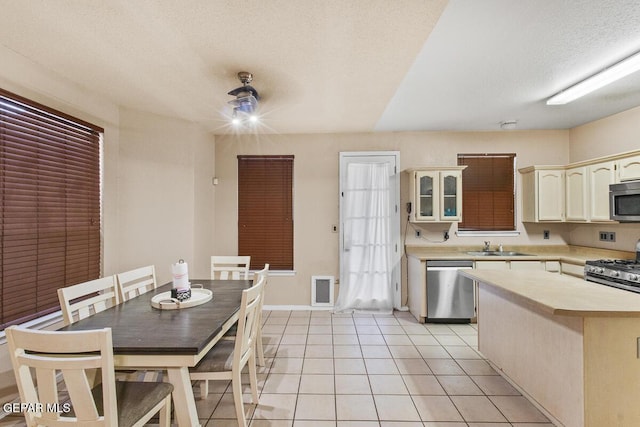 kitchen with appliances with stainless steel finishes, sink, light tile patterned floors, a kitchen island, and a textured ceiling