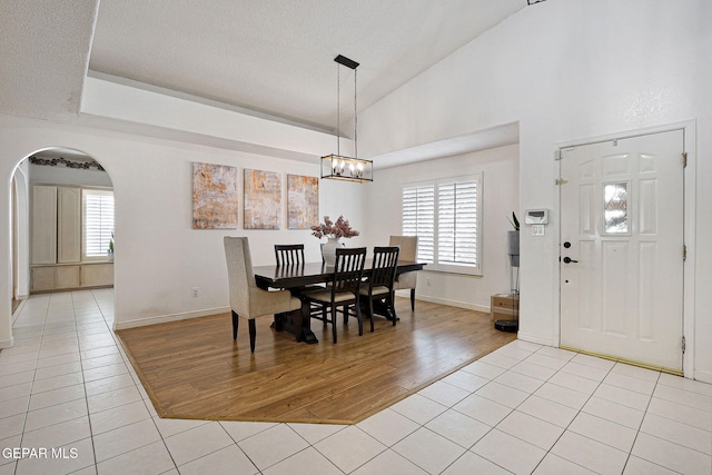 tiled dining space featuring an inviting chandelier, high vaulted ceiling, plenty of natural light, and a textured ceiling