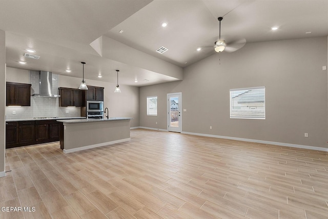 kitchen with a kitchen island with sink, visible vents, open floor plan, wall chimney exhaust hood, and stainless steel microwave