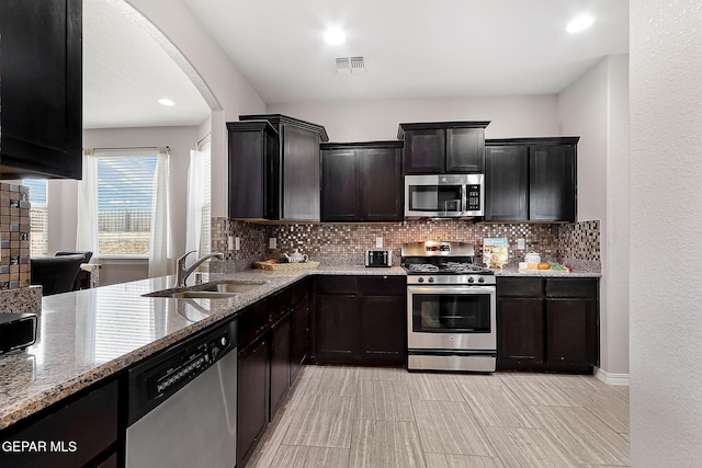 kitchen featuring visible vents, decorative backsplash, light stone counters, appliances with stainless steel finishes, and a sink