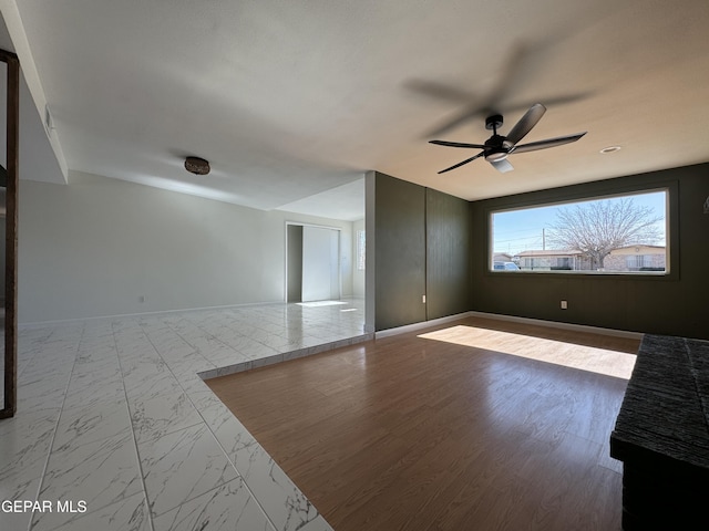 unfurnished living room featuring ceiling fan, marble finish floor, and baseboards