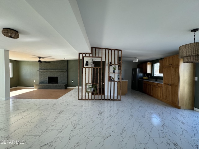 unfurnished living room featuring a ceiling fan, a brick fireplace, marble finish floor, and a sink