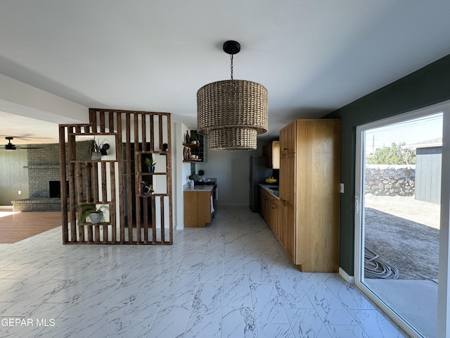 unfurnished dining area featuring ceiling fan with notable chandelier, marble finish floor, a brick fireplace, and baseboards