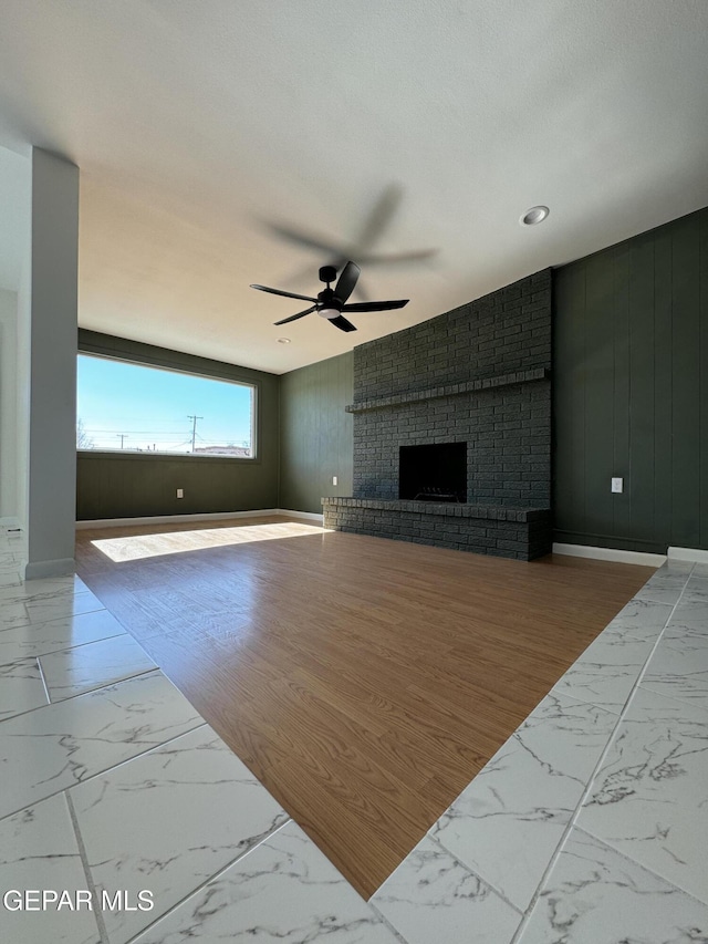 unfurnished living room with a ceiling fan, a brick fireplace, marble finish floor, and baseboards