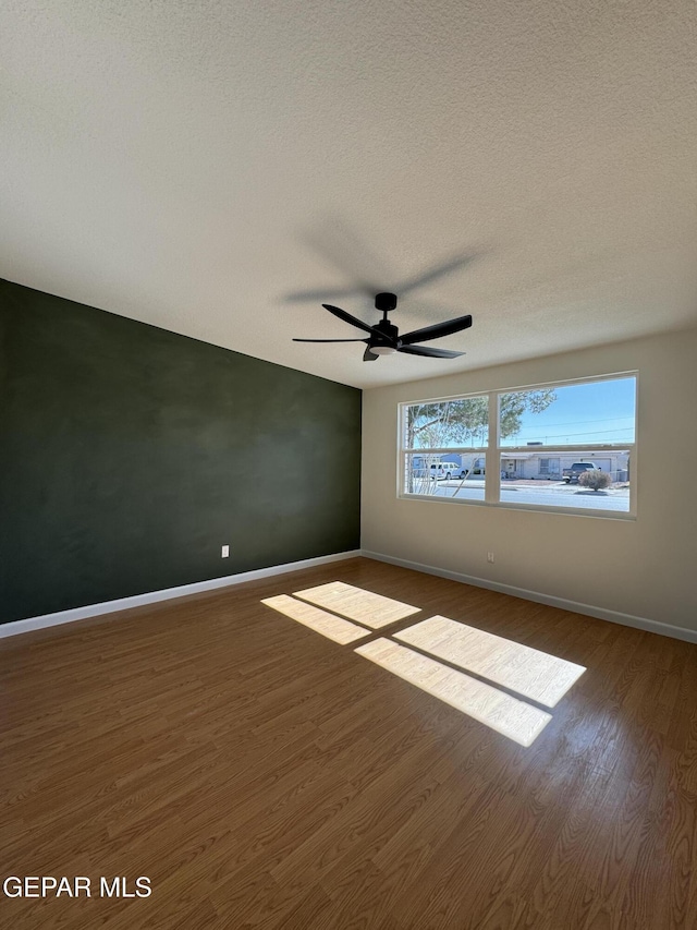 spare room featuring dark wood-style flooring, a textured ceiling, and baseboards