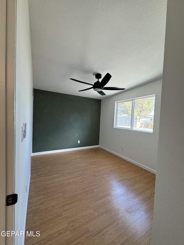 spare room with ceiling fan, a textured ceiling, baseboards, and wood finished floors