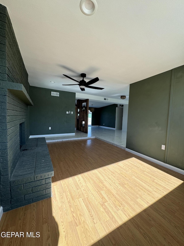 unfurnished living room featuring light wood finished floors, a fireplace, visible vents, and a ceiling fan