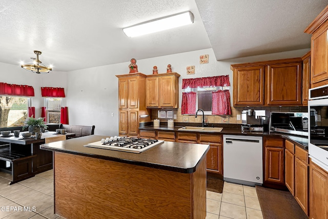 kitchen featuring a center island, dark countertops, brown cabinetry, a sink, and white appliances