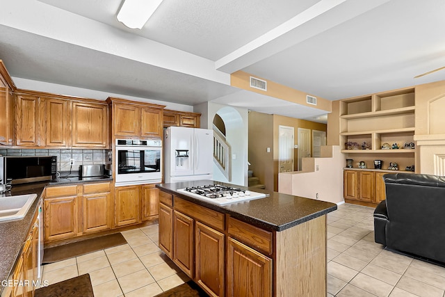 kitchen featuring light tile patterned floors, white appliances, a kitchen island, visible vents, and dark countertops