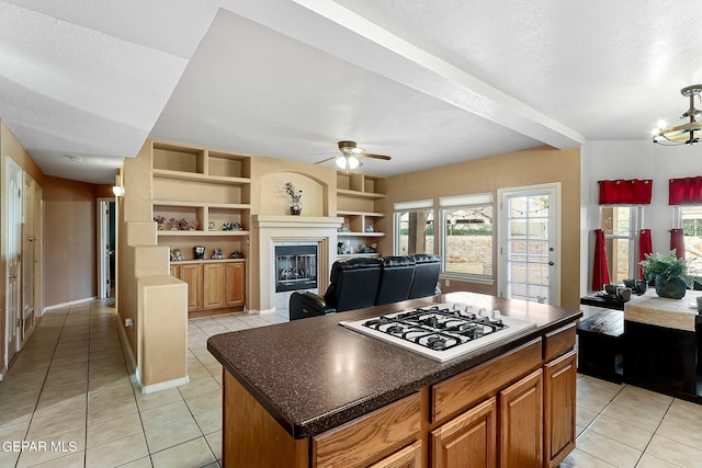 kitchen featuring dark countertops, a fireplace with flush hearth, open floor plan, a center island, and white gas cooktop