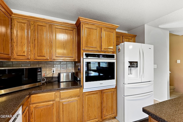 kitchen featuring white appliances, dark countertops, decorative backsplash, and brown cabinets