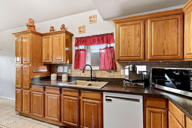 kitchen with dark countertops, stainless steel microwave, decorative backsplash, a sink, and dishwashing machine