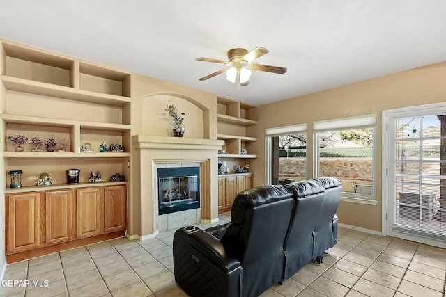 living area featuring built in shelves, a tiled fireplace, light tile patterned flooring, and a ceiling fan