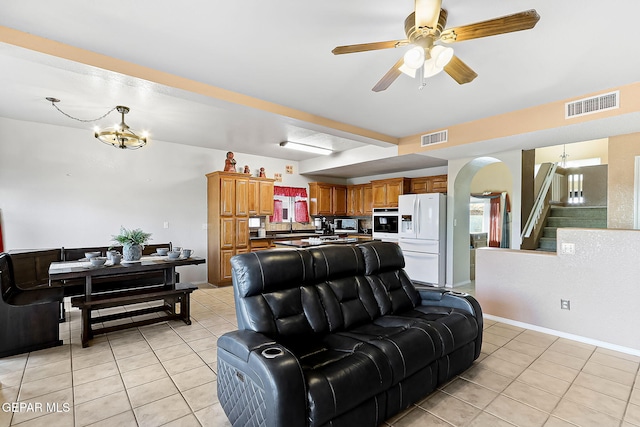 living area with ceiling fan with notable chandelier, stairs, visible vents, and light tile patterned flooring