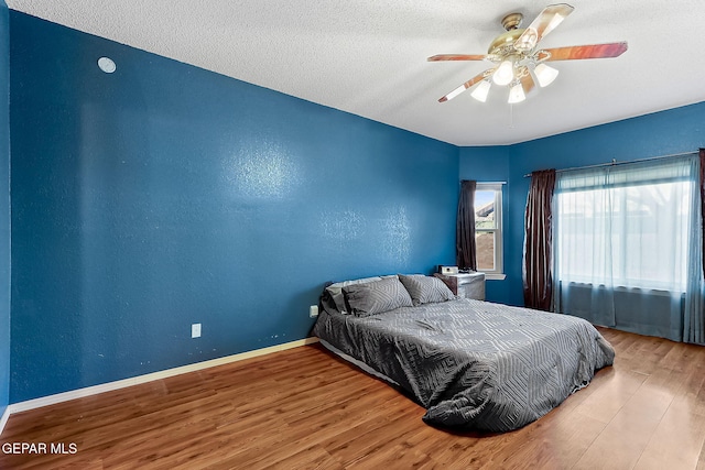 bedroom featuring ceiling fan, a textured wall, a textured ceiling, wood finished floors, and baseboards