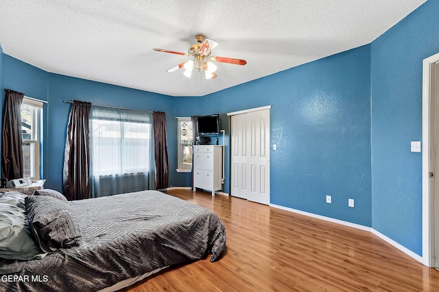 bedroom featuring a textured wall, a ceiling fan, a textured ceiling, wood finished floors, and baseboards