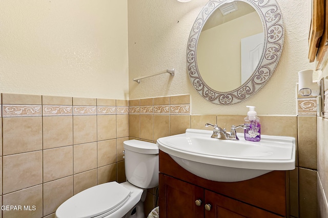 bathroom featuring visible vents, wainscoting, toilet, vanity, and tile walls