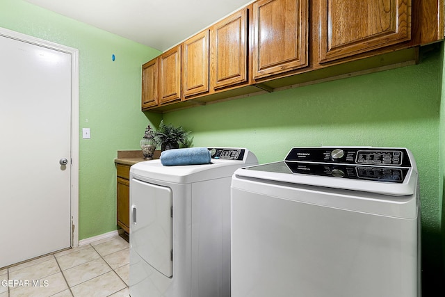 clothes washing area featuring cabinet space, light tile patterned floors, and washer and clothes dryer