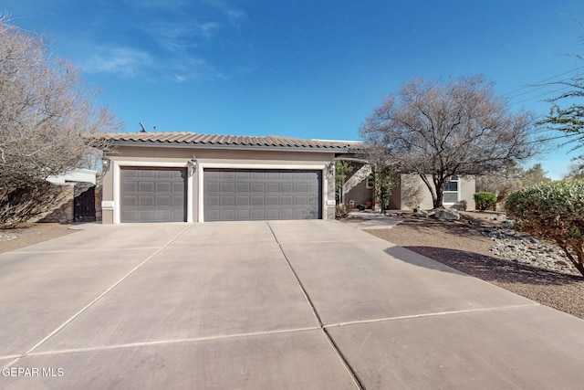 view of front facade featuring a garage, driveway, a tiled roof, and stucco siding