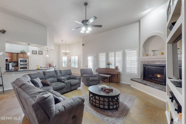 living room featuring ceiling fan with notable chandelier, a high ceiling, a fireplace, and baseboards