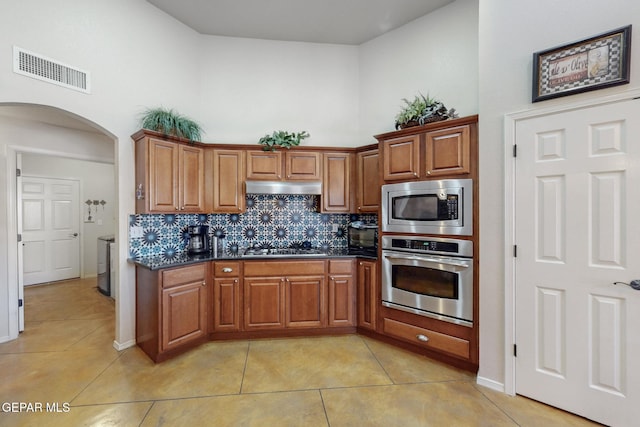 kitchen featuring arched walkways, brown cabinets, stainless steel appliances, visible vents, and under cabinet range hood