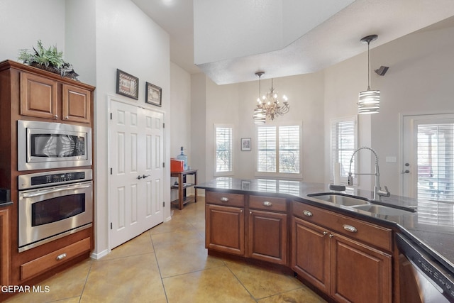 kitchen with a sink, appliances with stainless steel finishes, brown cabinets, dark countertops, and pendant lighting