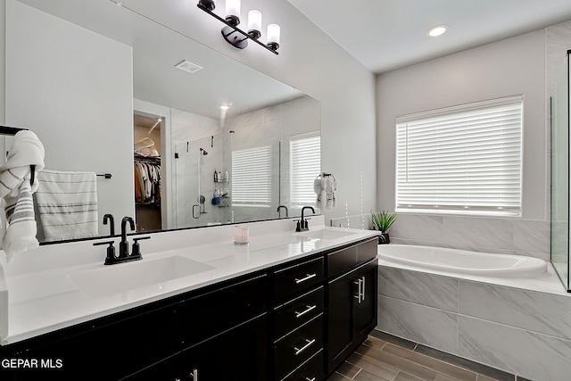 bathroom featuring a garden tub, visible vents, a walk in closet, and a sink