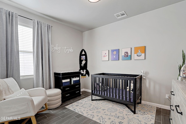 bedroom with wood tiled floor, baseboards, visible vents, and a nursery area