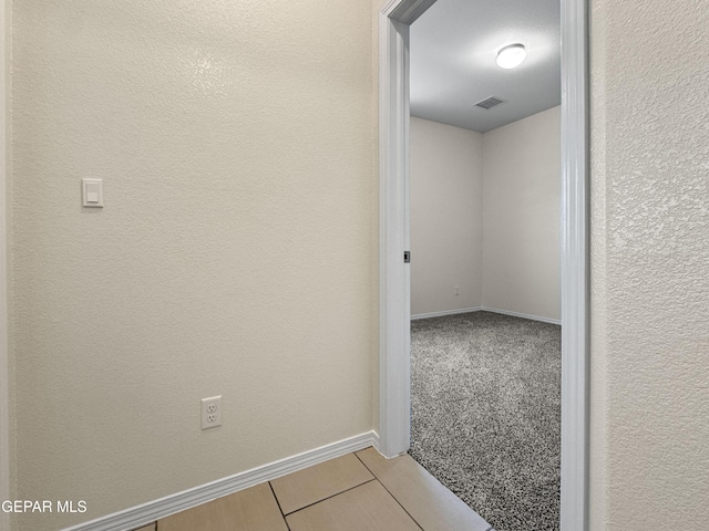 hallway featuring carpet floors, visible vents, a textured wall, and baseboards