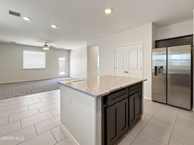 kitchen featuring stainless steel fridge, visible vents, ceiling fan, a kitchen island, and light stone countertops