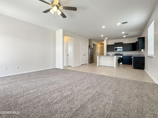 kitchen featuring light carpet, open floor plan, dark cabinets, a center island, and stainless steel appliances