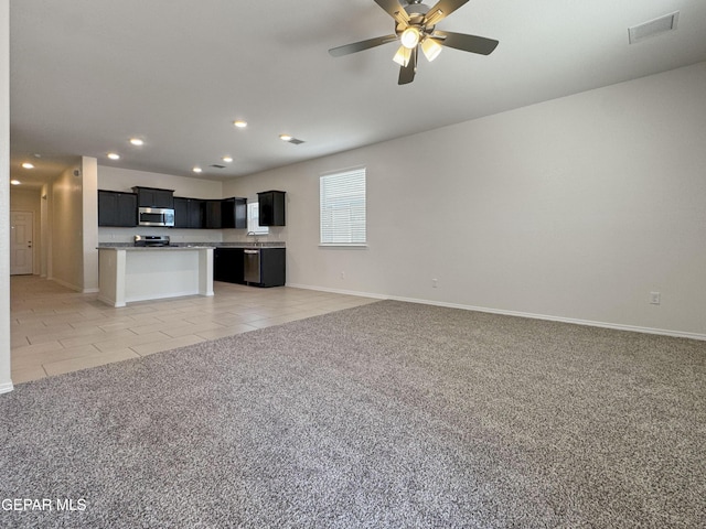 kitchen with light tile patterned floors, light carpet, open floor plan, appliances with stainless steel finishes, and dark cabinetry