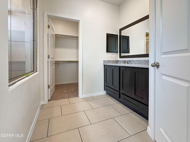 full bath with a walk in closet, vanity, baseboards, and tile patterned floors