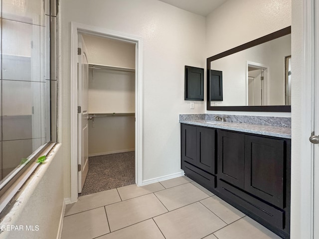 full bathroom with baseboards, a walk in closet, vanity, and tile patterned floors