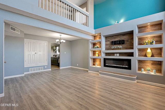 unfurnished living room featuring built in features, visible vents, wood finished floors, a chandelier, and baseboards