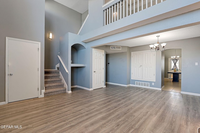 unfurnished living room featuring visible vents, baseboards, wood finished floors, stairs, and a notable chandelier