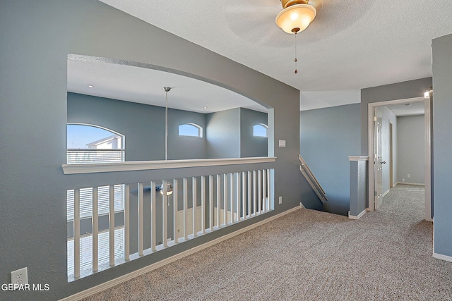 hallway with carpet, baseboards, a textured ceiling, and an upstairs landing