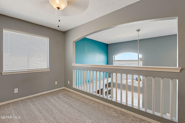 carpeted spare room featuring a textured ceiling, a ceiling fan, and baseboards