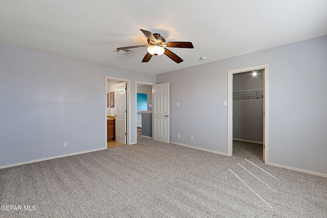 unfurnished bedroom featuring light colored carpet, a spacious closet, baseboards, and a textured ceiling