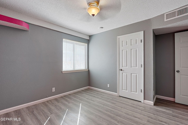 unfurnished bedroom featuring a textured ceiling, a textured wall, visible vents, baseboards, and light wood-style floors