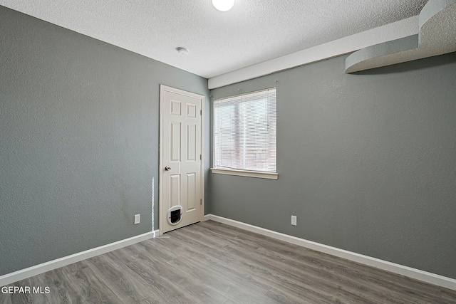 spare room featuring a textured ceiling, baseboards, wood finished floors, and a textured wall