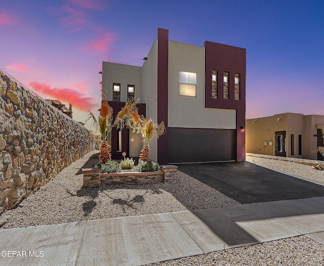 view of front facade with an attached garage, fence, aphalt driveway, and stucco siding