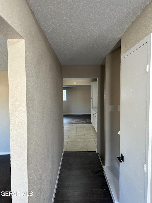 corridor with a textured ceiling, baseboards, wood finished floors, and a textured wall