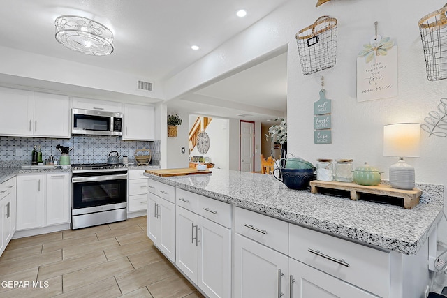 kitchen featuring light stone counters, visible vents, backsplash, appliances with stainless steel finishes, and white cabinetry