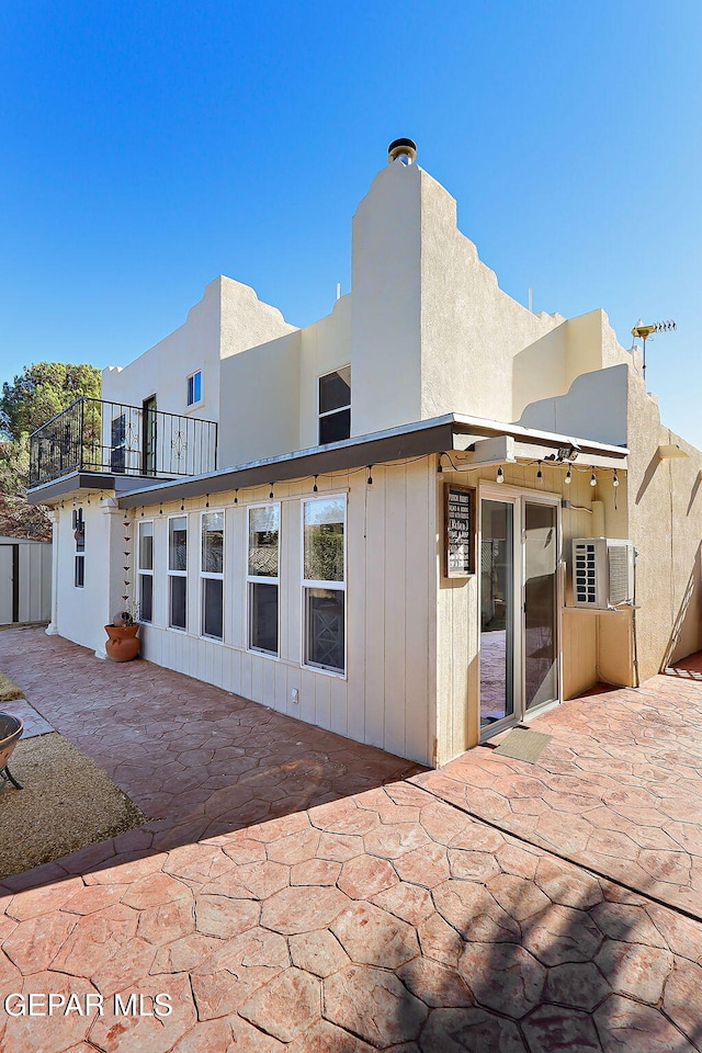 rear view of house featuring a balcony, stucco siding, and a patio