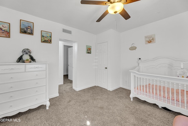 bedroom featuring a crib, baseboards, visible vents, a ceiling fan, and light colored carpet