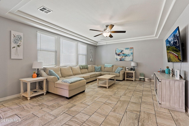 living area with a raised ceiling, visible vents, a ceiling fan, and baseboards