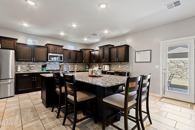 kitchen featuring light stone counters, visible vents, decorative backsplash, appliances with stainless steel finishes, and a breakfast bar area